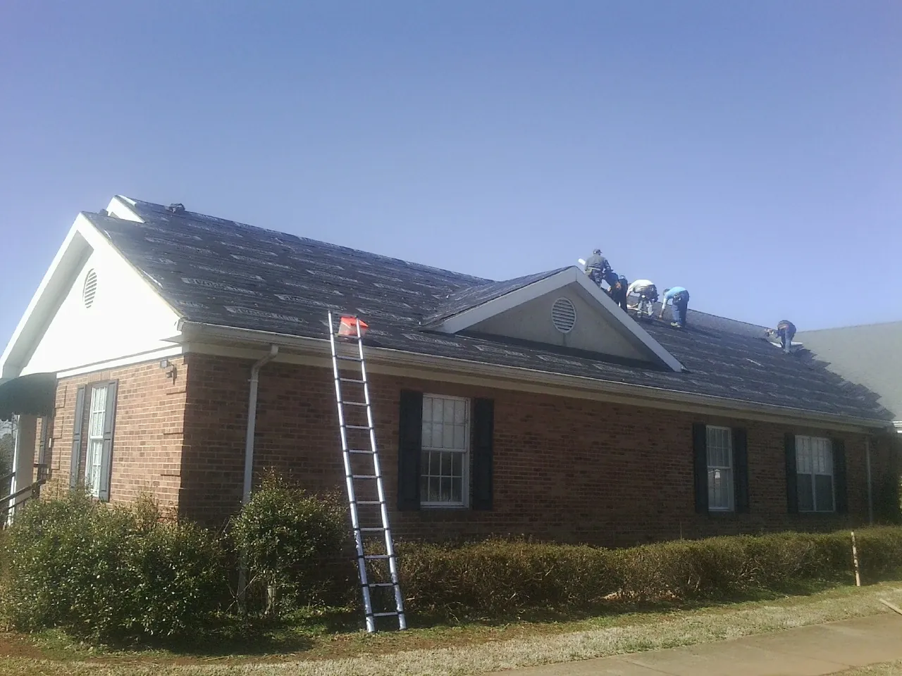 Crew tearing shingles off a brick ranch roof with a ladder set — Emergency Roof Repair work by our crew in West Chester