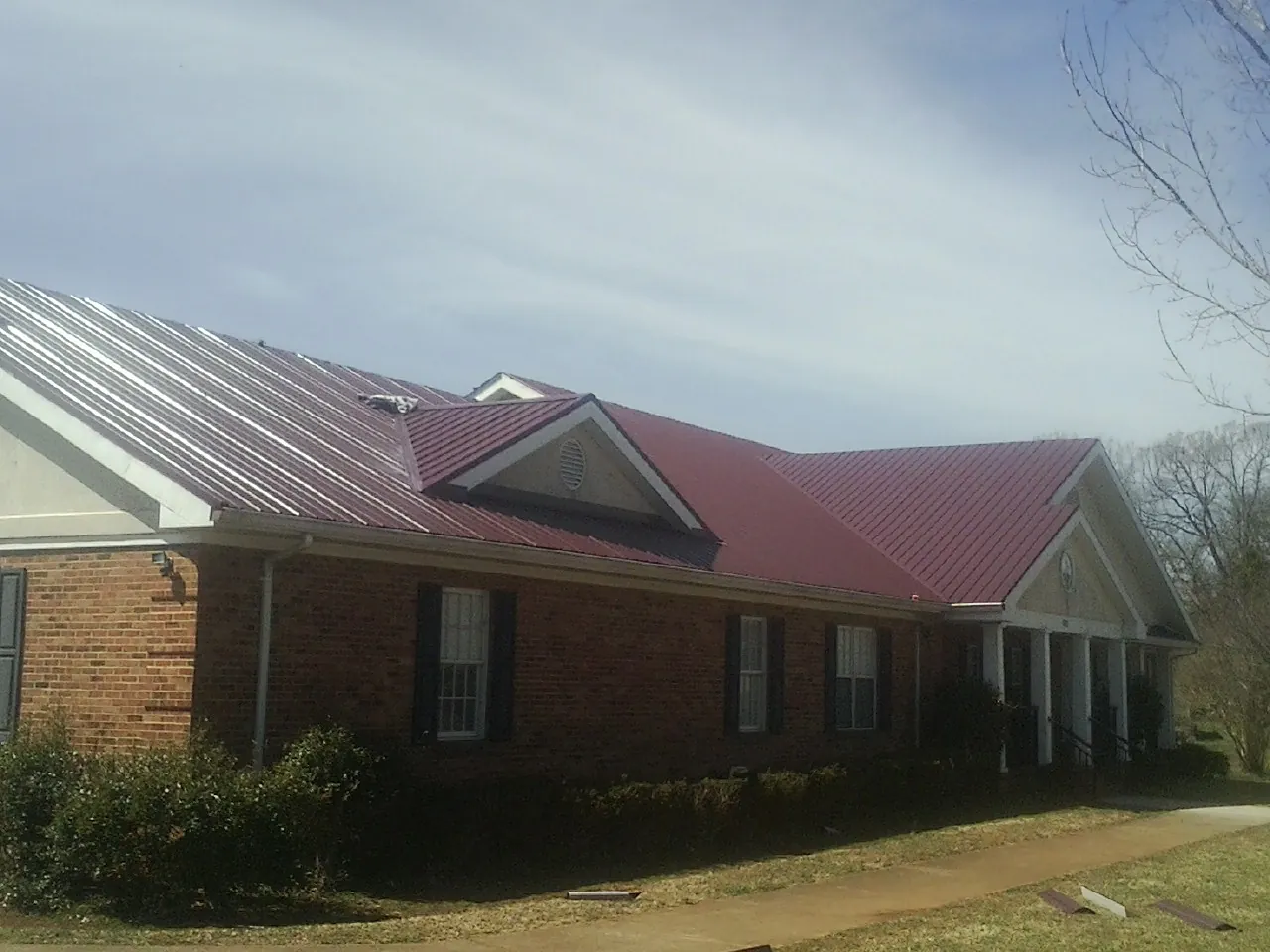 Red metal roof with gabled entries on a long brick building, from a Hail Damage Roof Repair job in West Chester