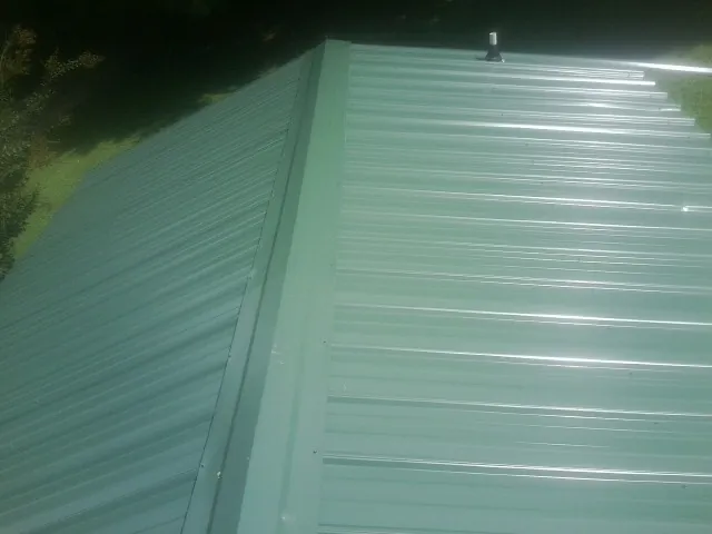 New green metal panels meeting at the ridge of a roof — Flat Roof Repair work by our crew in West Chester