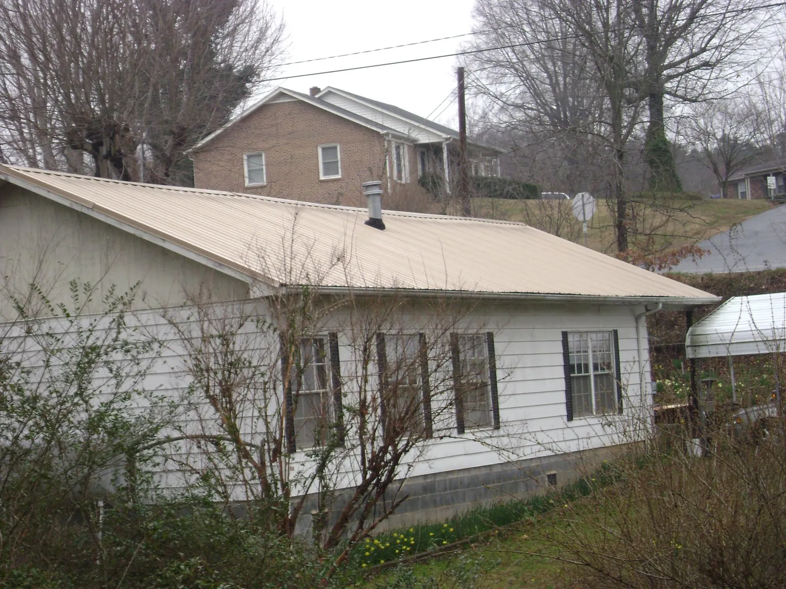 Tan metal roof on a white sided house set into a hillside — Commercial Roofing by Roofing Brothers in West Chester